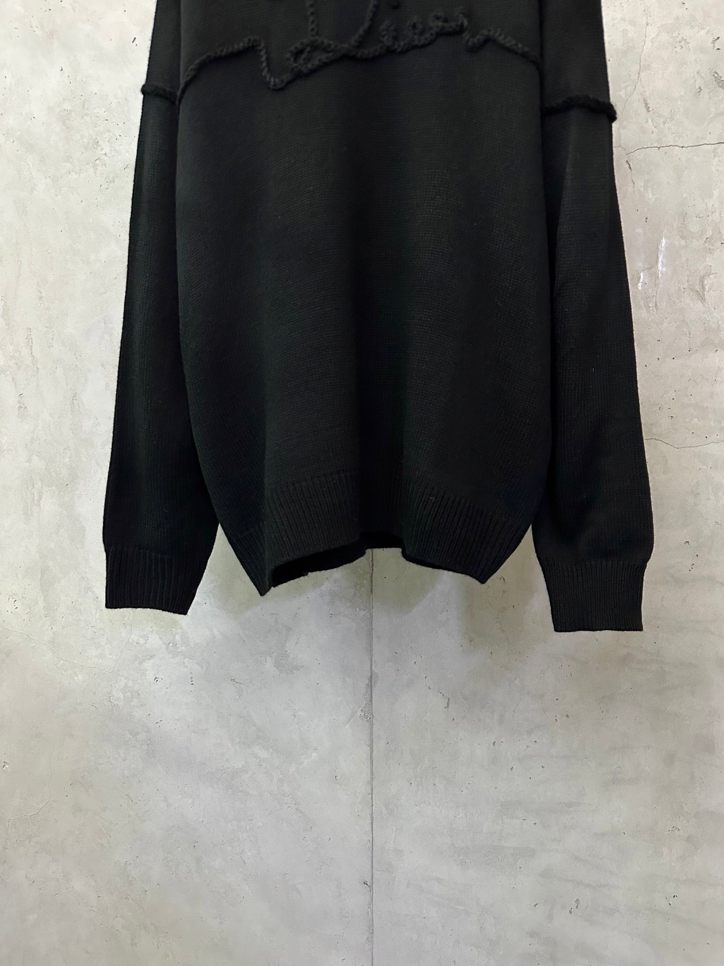 Black knit sweater hem and cuffs detail, featuring embroidered chest logo panel
