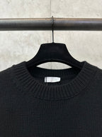 Black crew-neck knit sweater close-up with ribbed collar and inside neck label
