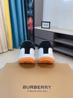 Back view of white sneakers with dark heel panels and orange rubber outsoles