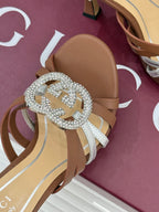 Gucci heeled sandal close-up: jeweled G buckle on metallic silver straps, tan sole