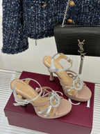 Gucci heeled sandals pair showing side straps and crystal-style heart buckle on light beige