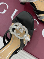 Gucci heeled sandal close-up of rhinestone buckle with dark center on black strap