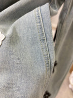 Close-up of light wash denim pants with small cross patch near seam