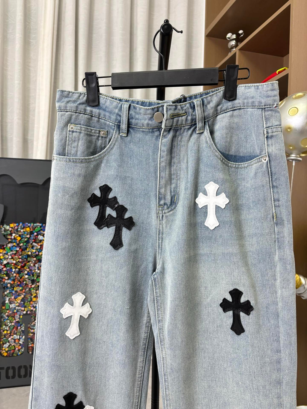 Light wash denim pants with button fly and black cross patches