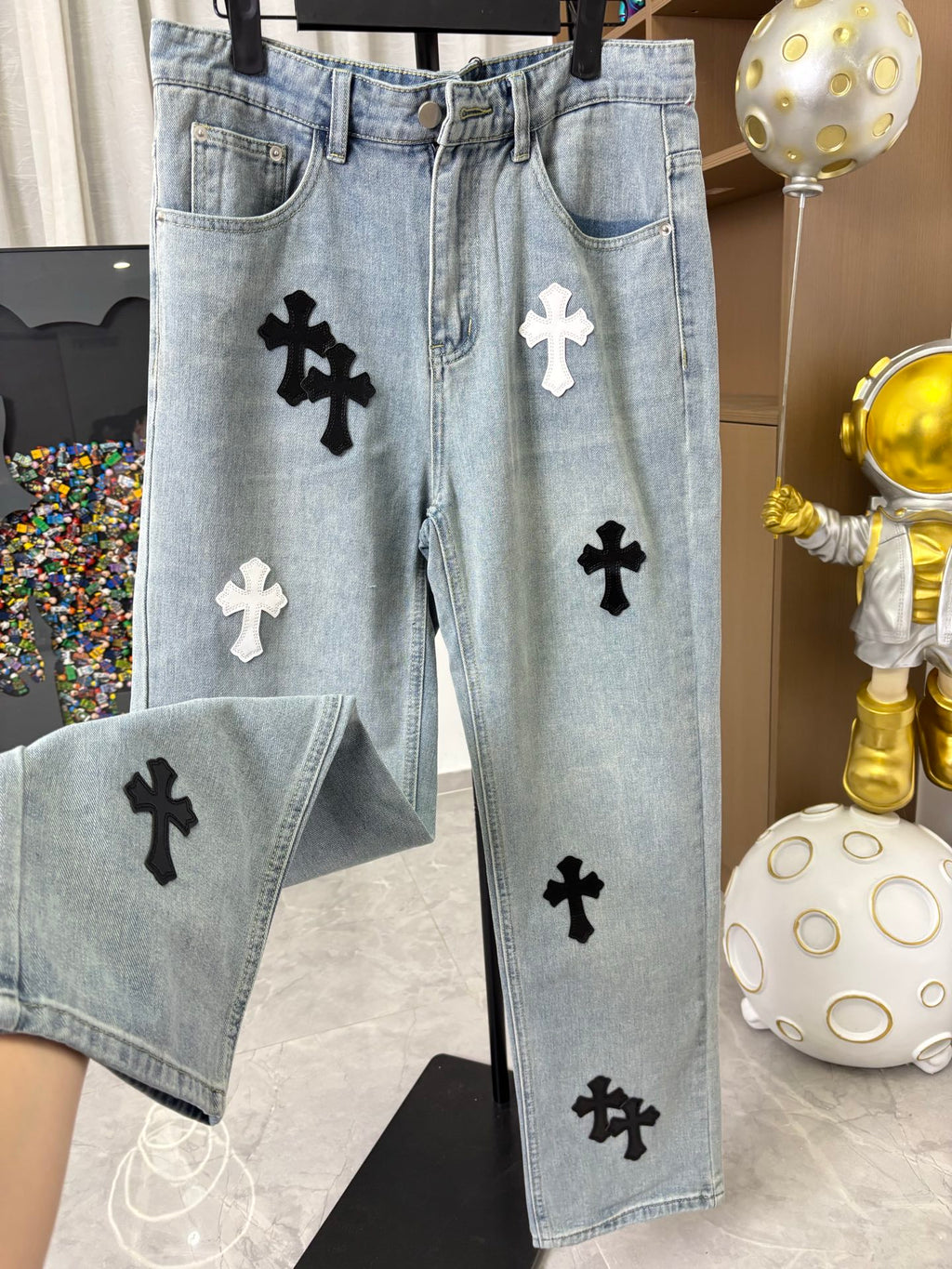 Light wash denim pants featuring scattered black and white cross patches