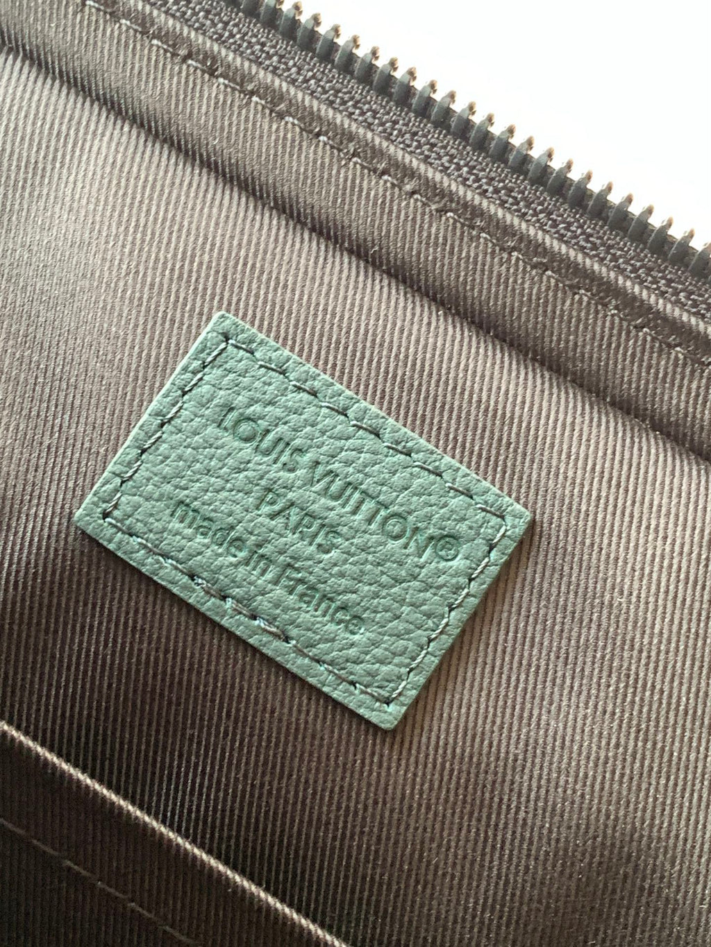 Louis Vuitton men's bag lining label in green, stitched fabric tag close-up