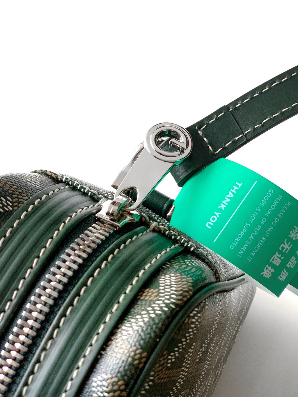 Green bag close-up with zipper pulls, ring hardware, and teal brand tag on strap