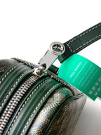 Green bag close-up with zipper pulls, ring hardware, and teal brand tag on strap