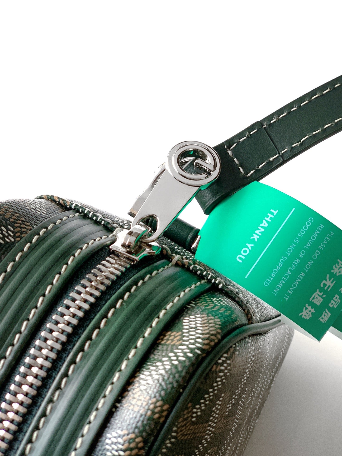 Green bag close-up with zipper pulls, ring hardware, and teal brand tag on strap