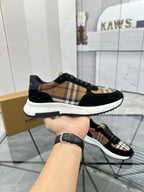 Burberry sneakers held by hand: black suede, tartan check stripe, white outsole