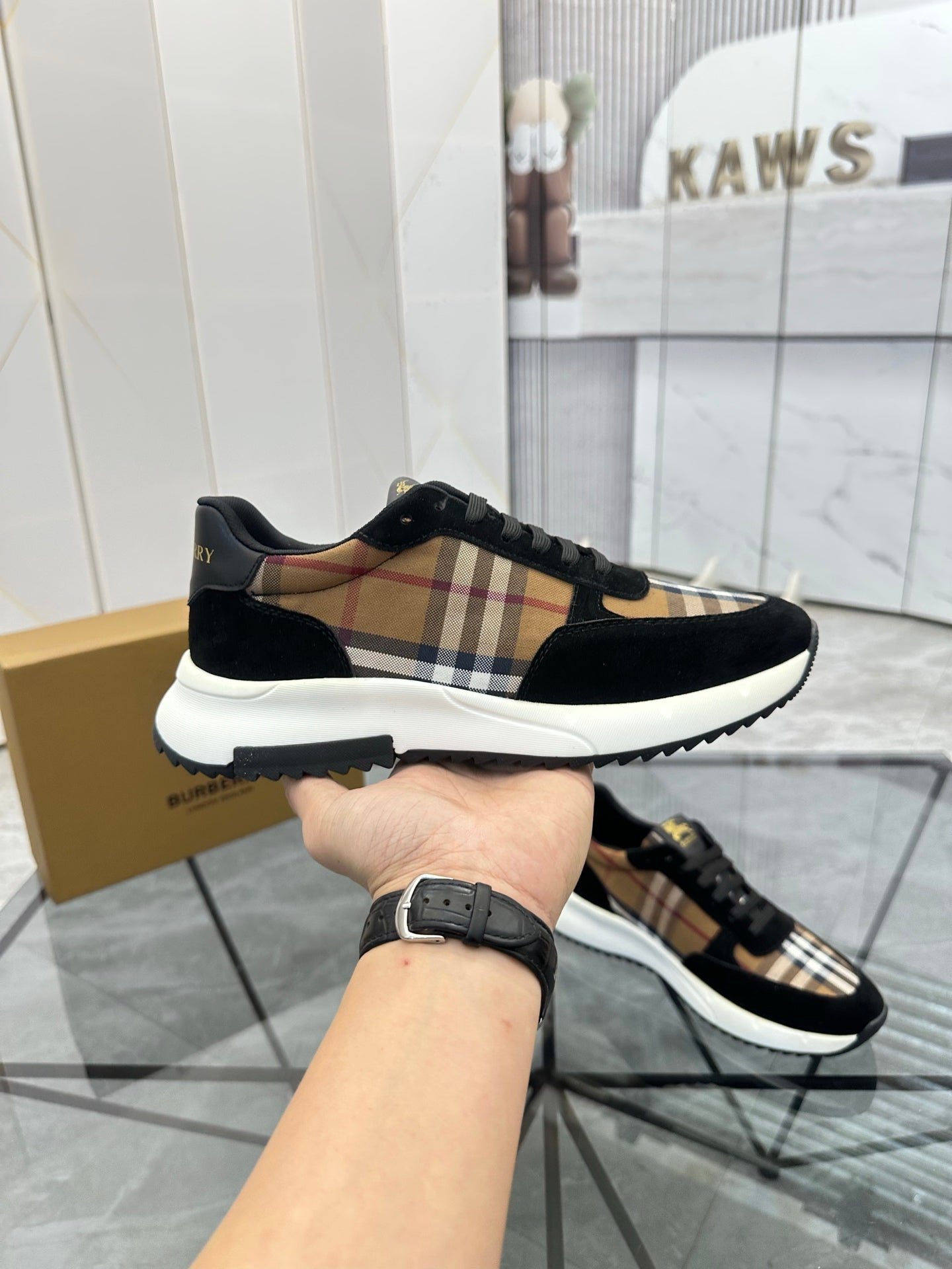 Burberry sneakers held by hand: black suede, tartan check stripe, white outsole