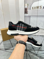 Burberry black lace-up sneaker held in hand, showing tartan stripe and white outsole