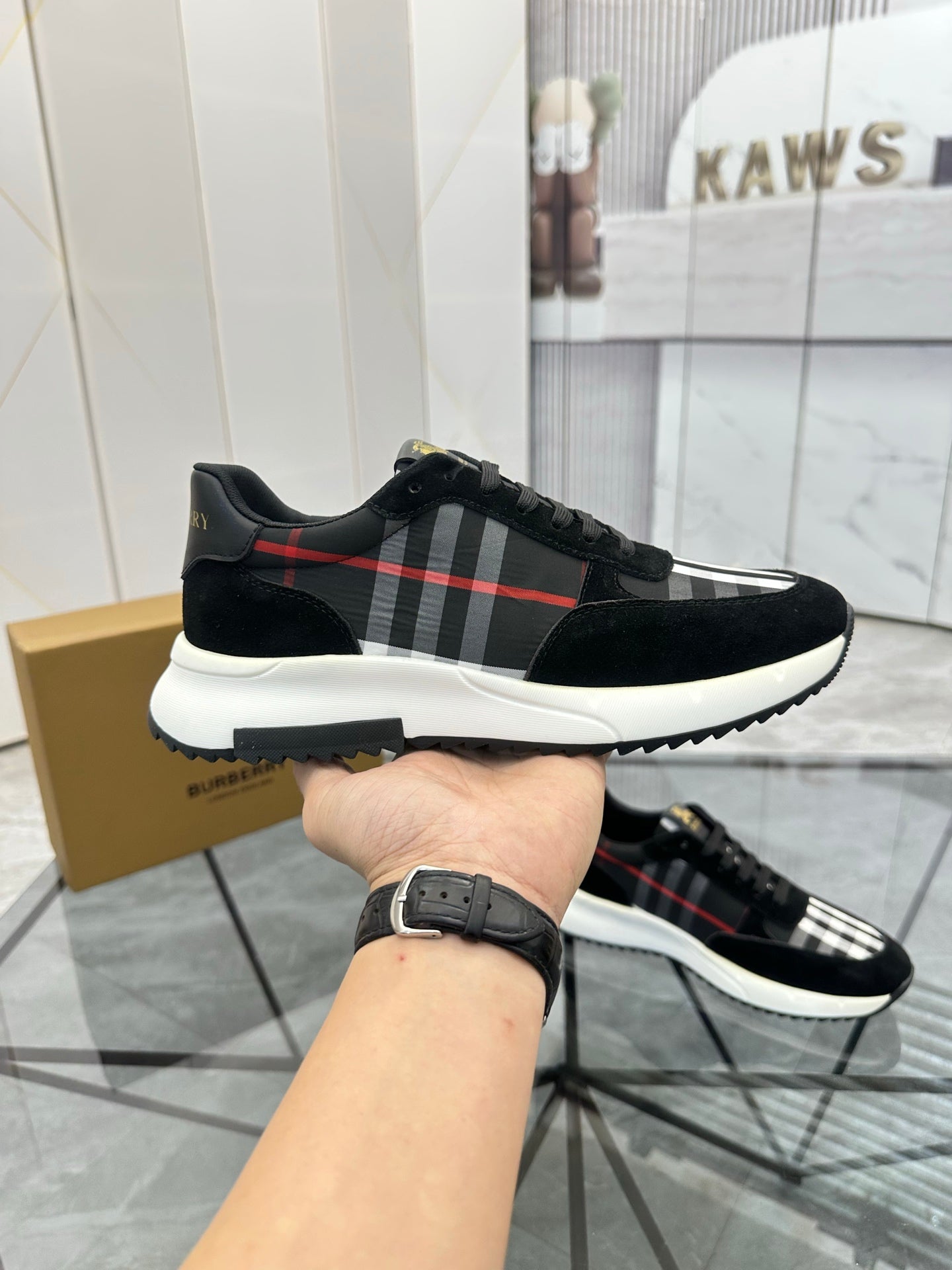 Burberry black lace-up sneaker held in hand, showing tartan stripe and white outsole
