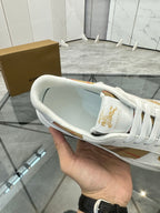 White sneaker interior view showing gold heel logo and white laces, rubber sole