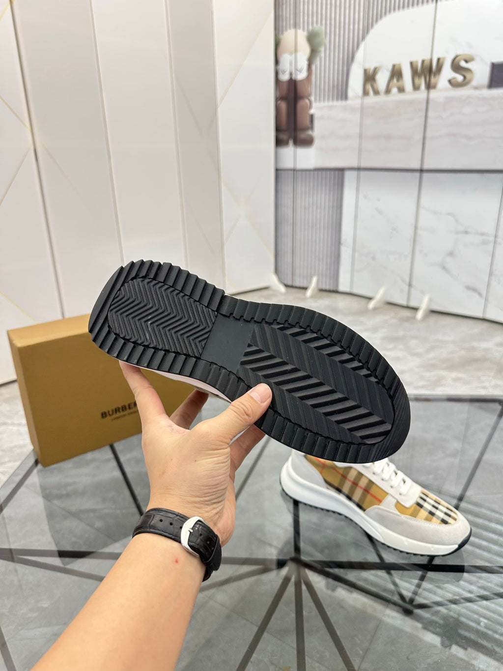 Black rubber outsole view of sneaker with tread pattern, held in hand