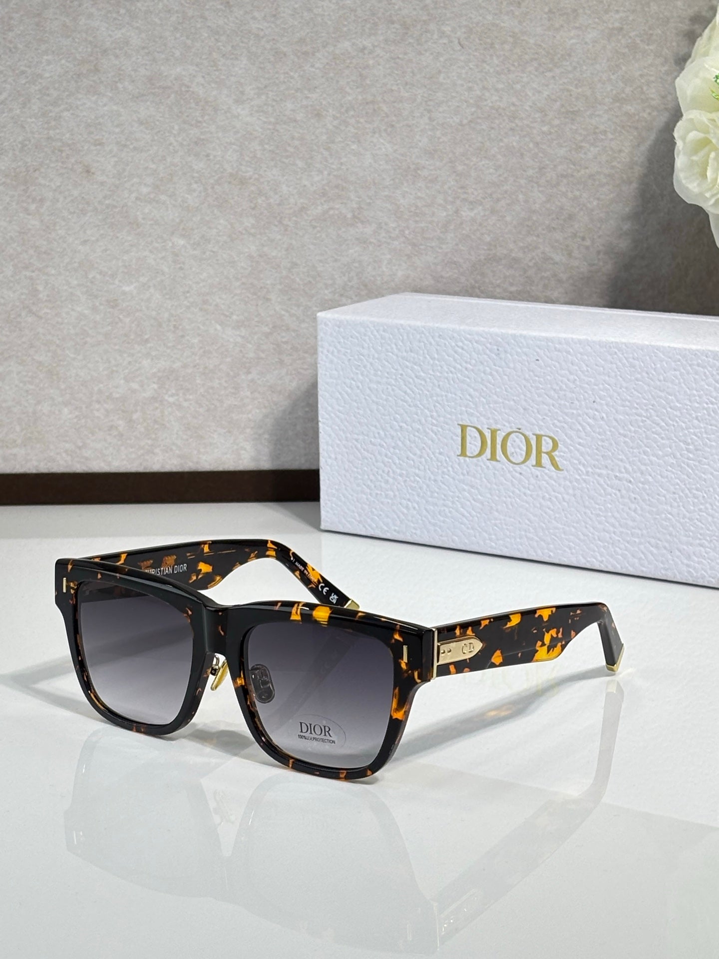 Dior sunglasses with tortoiseshell frames and dark lenses, gold logo accents on the sides