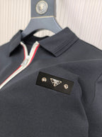 Black polo shirt with collar and gold Prada logo patch at chest.