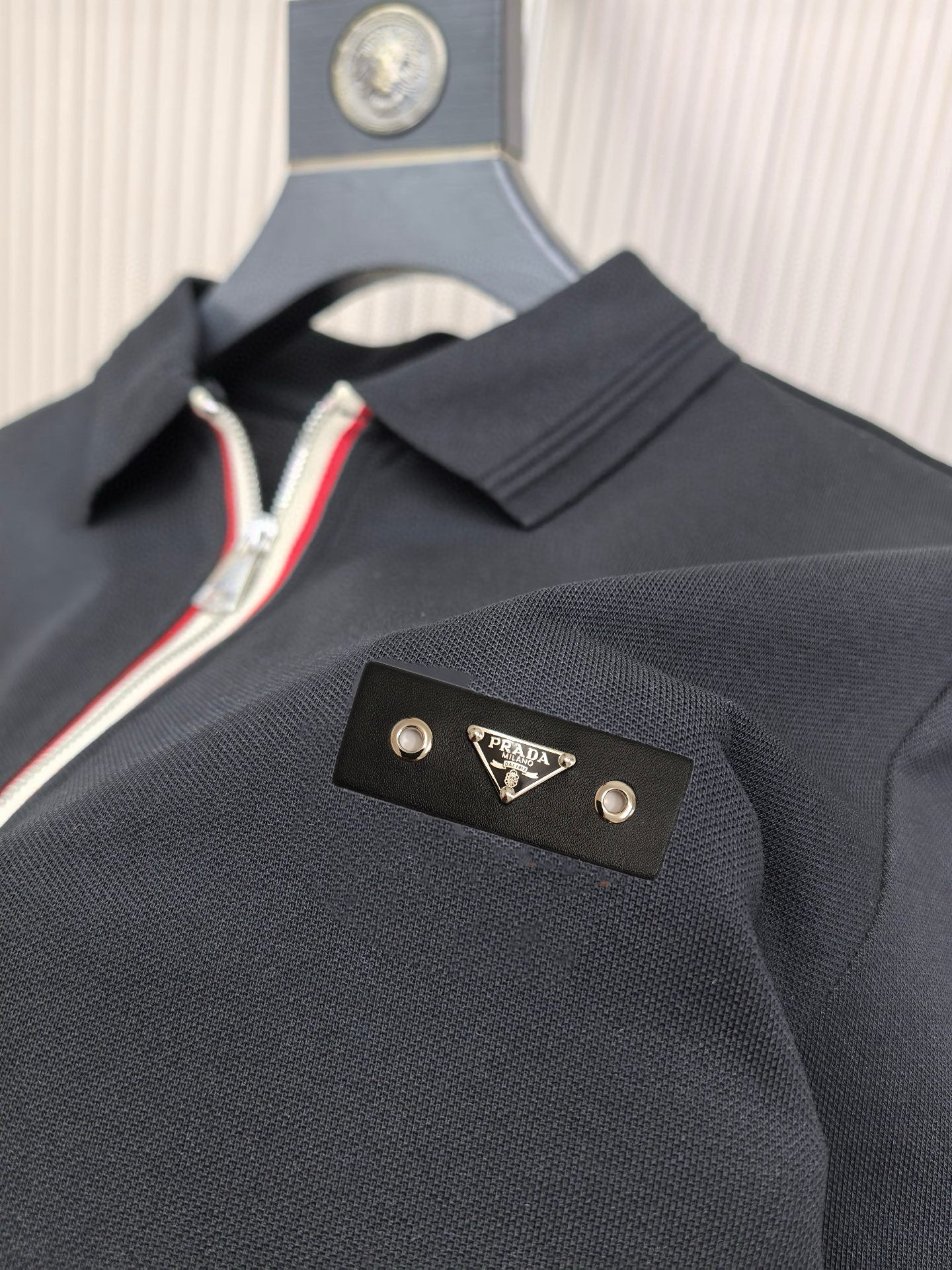 Black polo shirt with collar and gold Prada logo patch at chest.