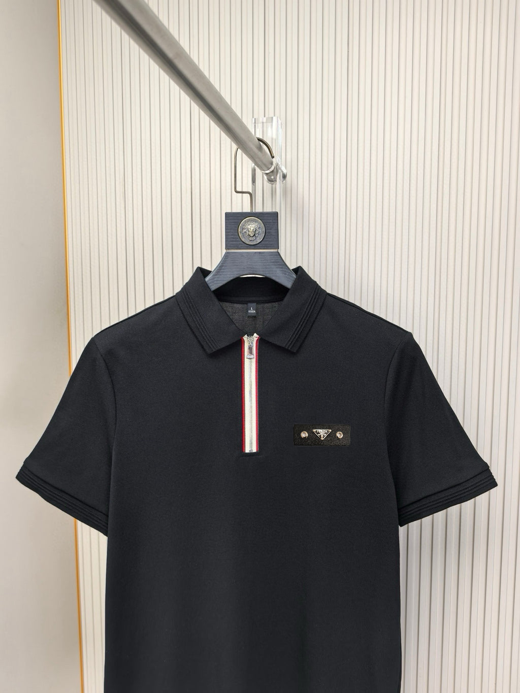 Black short-sleeve polo shirt with striped zip pull and chest logo.