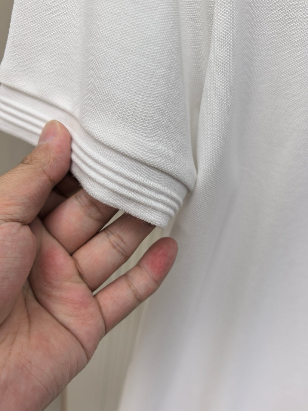 Hand holding the folded hem of a white polo shirt sleeve cuff