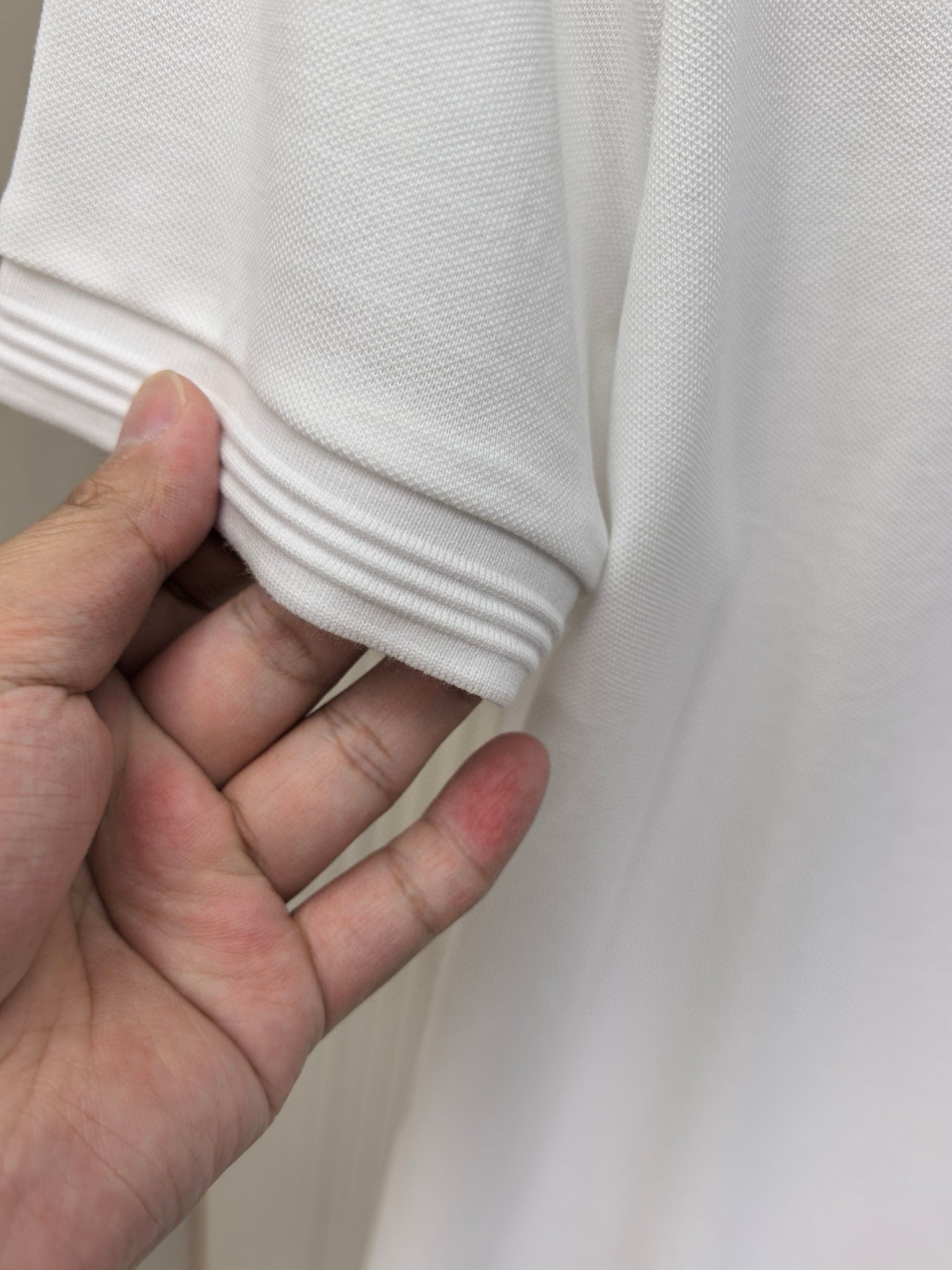 Close-up of white polo shirt sleeve cuff with ribbed knit hem detail.