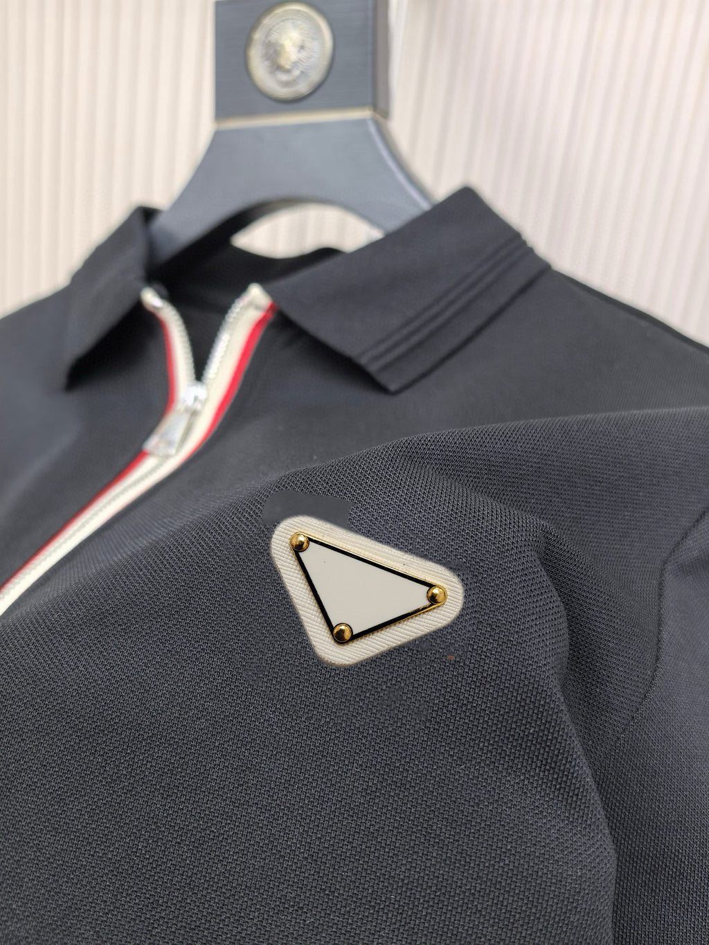 Black polo shirt with triangular logo patch and striped zipper trim
