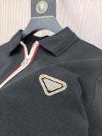 Black polo shirt with triangular logo patch and striped zipper trim