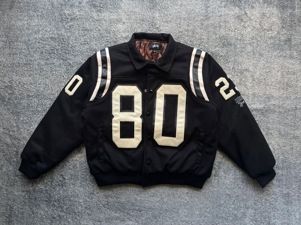 Black varsity jacket with white-striped sleeves and large “80” front patch