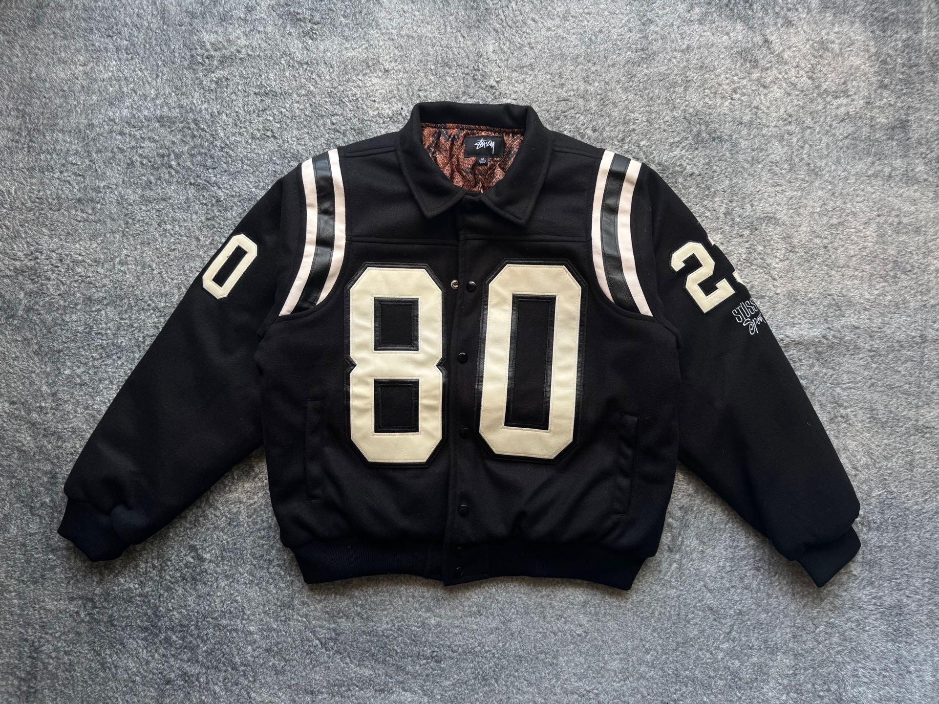 Black varsity jacket with white-striped sleeves and large “80” front patch