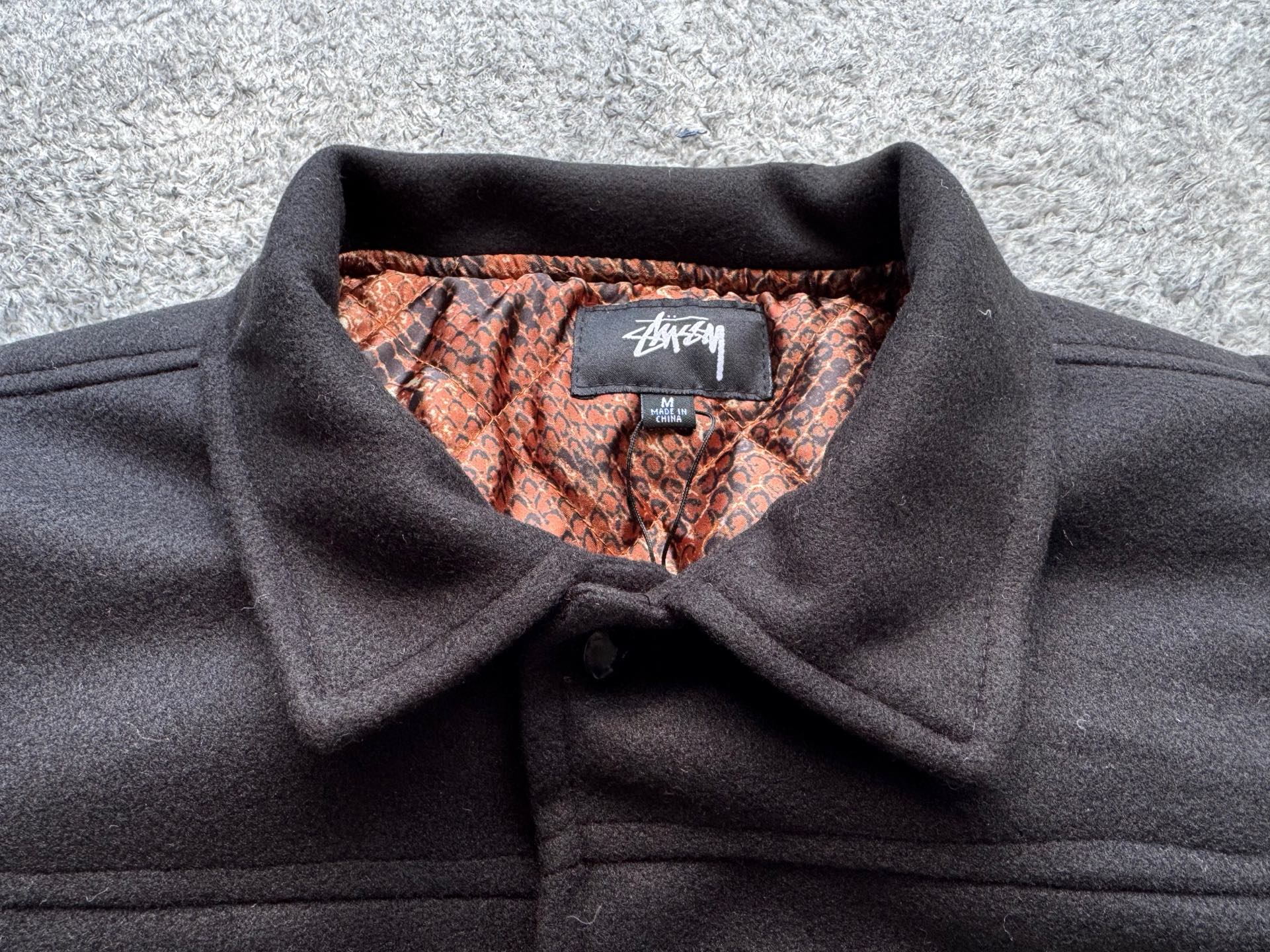 Black varsity jacket collar with orange-and-brown snake-print lining and brand label
