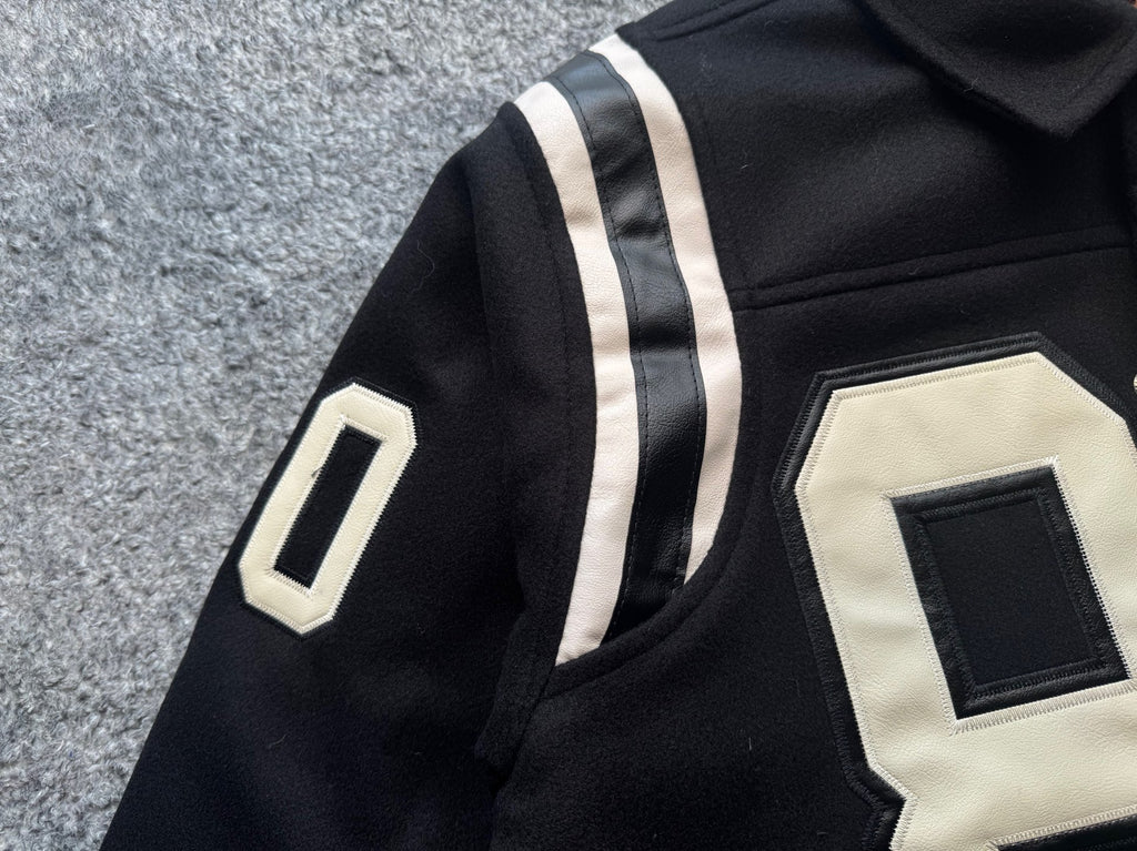 Black varsity jacket sleeve with white stripe and white appliqué “0” patch