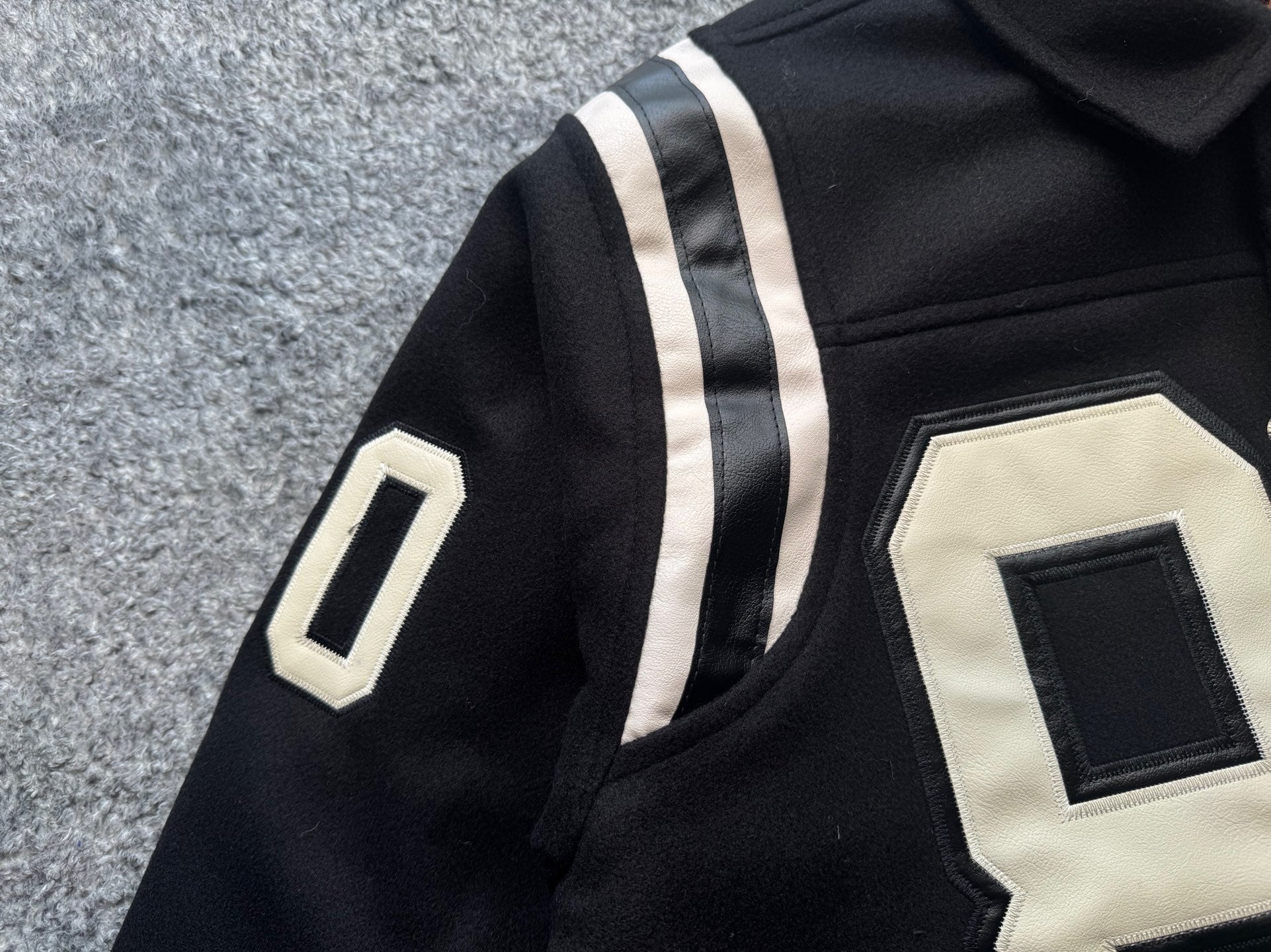 Black varsity jacket sleeve with white stripe and white appliqué “0” patch