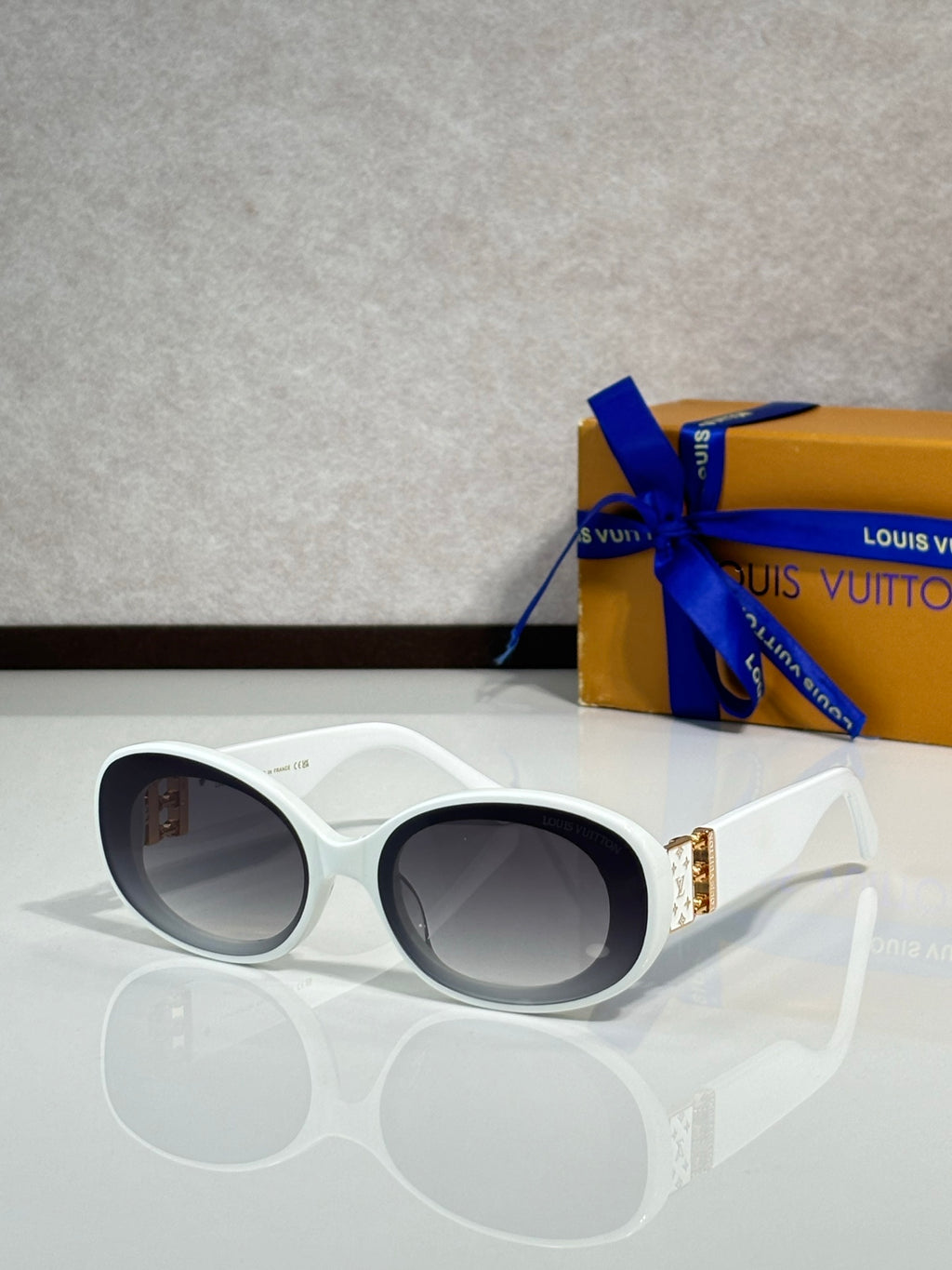 White oval sunglasses with dark lenses and gold LV logo on temple