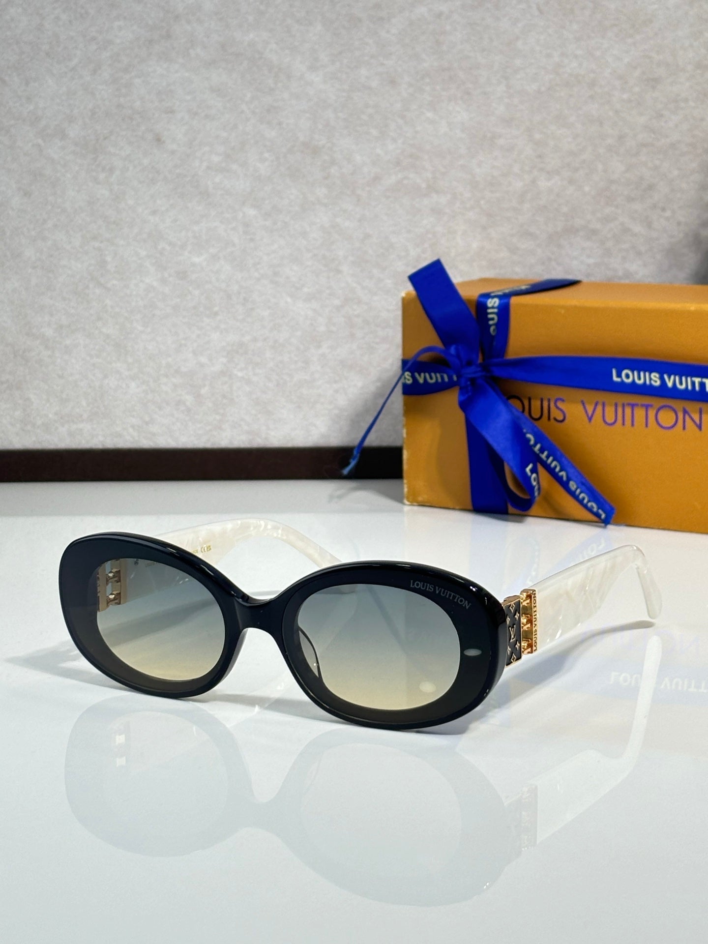Black oval sunglasses with pale lenses and gold LV logo on temple