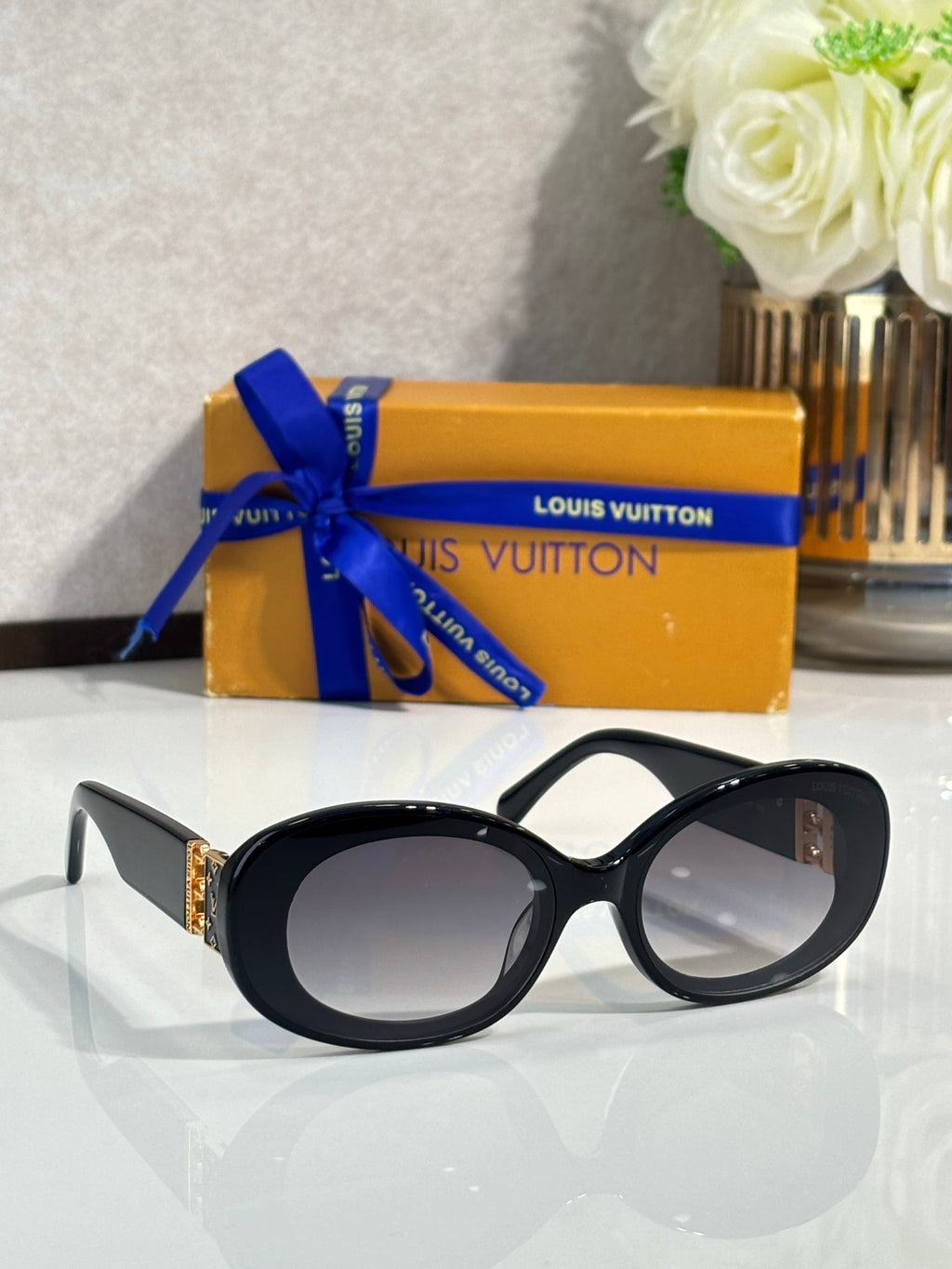 Black oval sunglasses with dark lenses and gold LV logo on temple