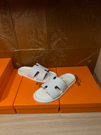 Hermes white slide sandals with smooth H-style strap cutouts, angled view