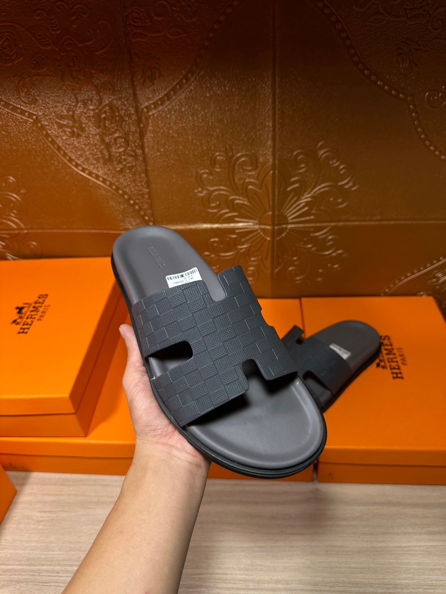 Hand holding a dark blue slide sandal with textured cross strap and open toe