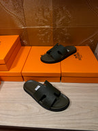 Hermes slide sandals, dark green pair placed on floor in front of orange boxes