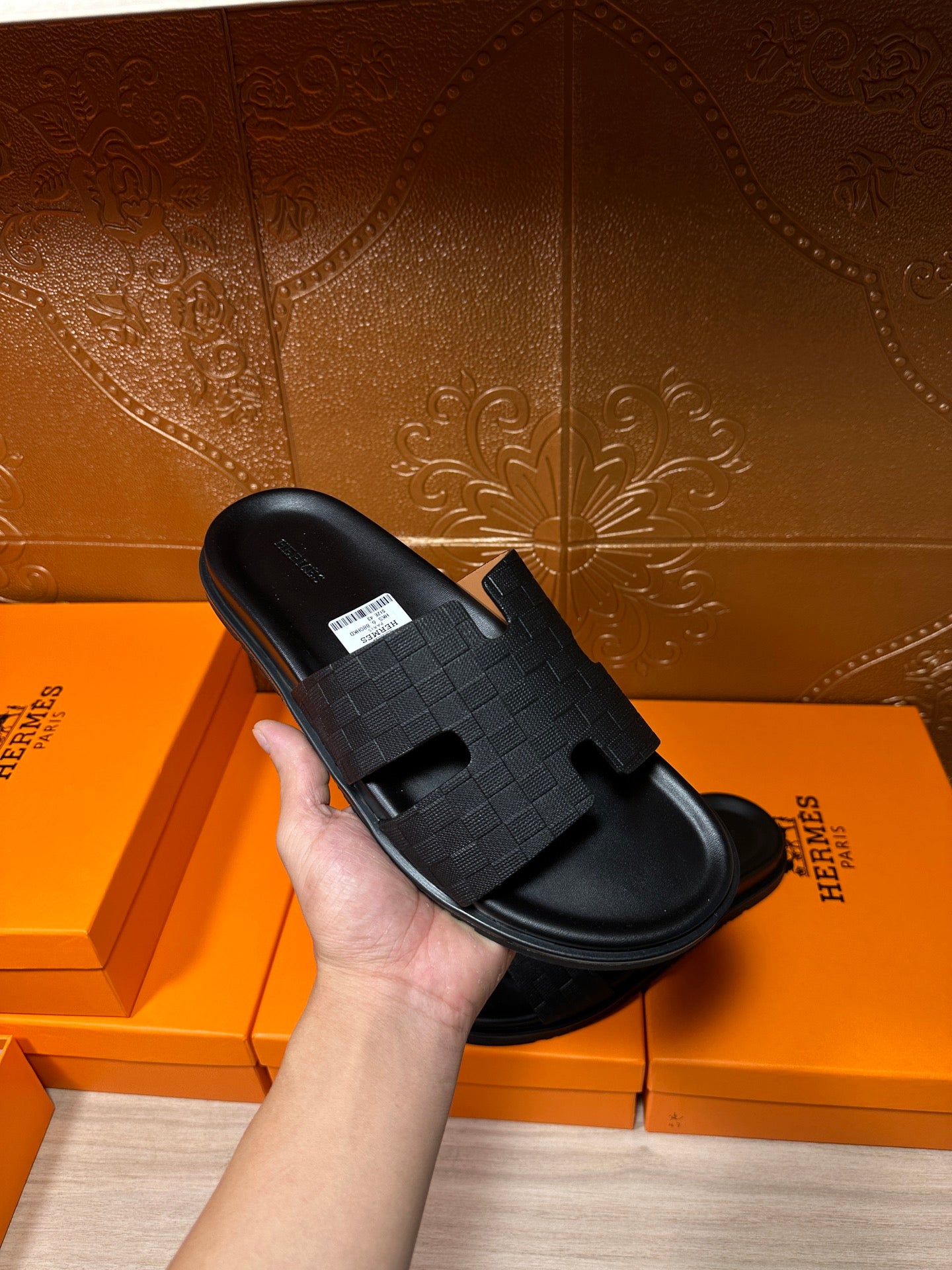 Black slide sandal held in hand, textured strap with open-toe slip-on design