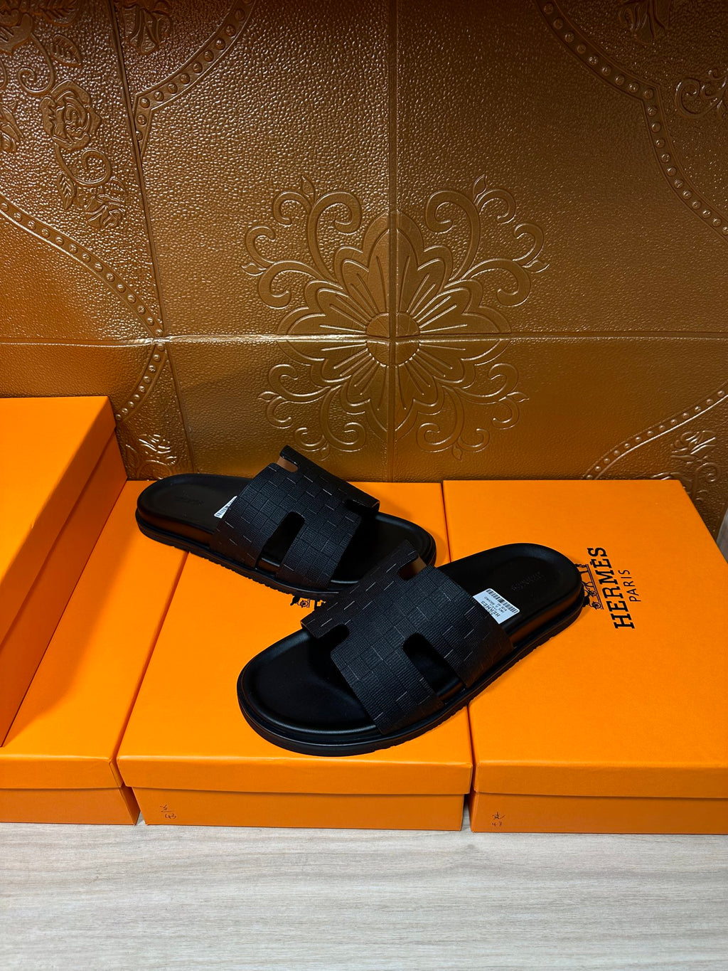 Black slide sandals with textured cross-strap and open-toe design on orange box