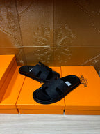 Black slide sandals with textured cross-strap and open-toe design on orange box