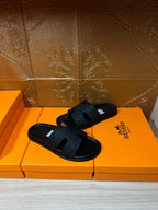 Black slide sandals with woven-pattern straps, open-toe design on orange Hermes box