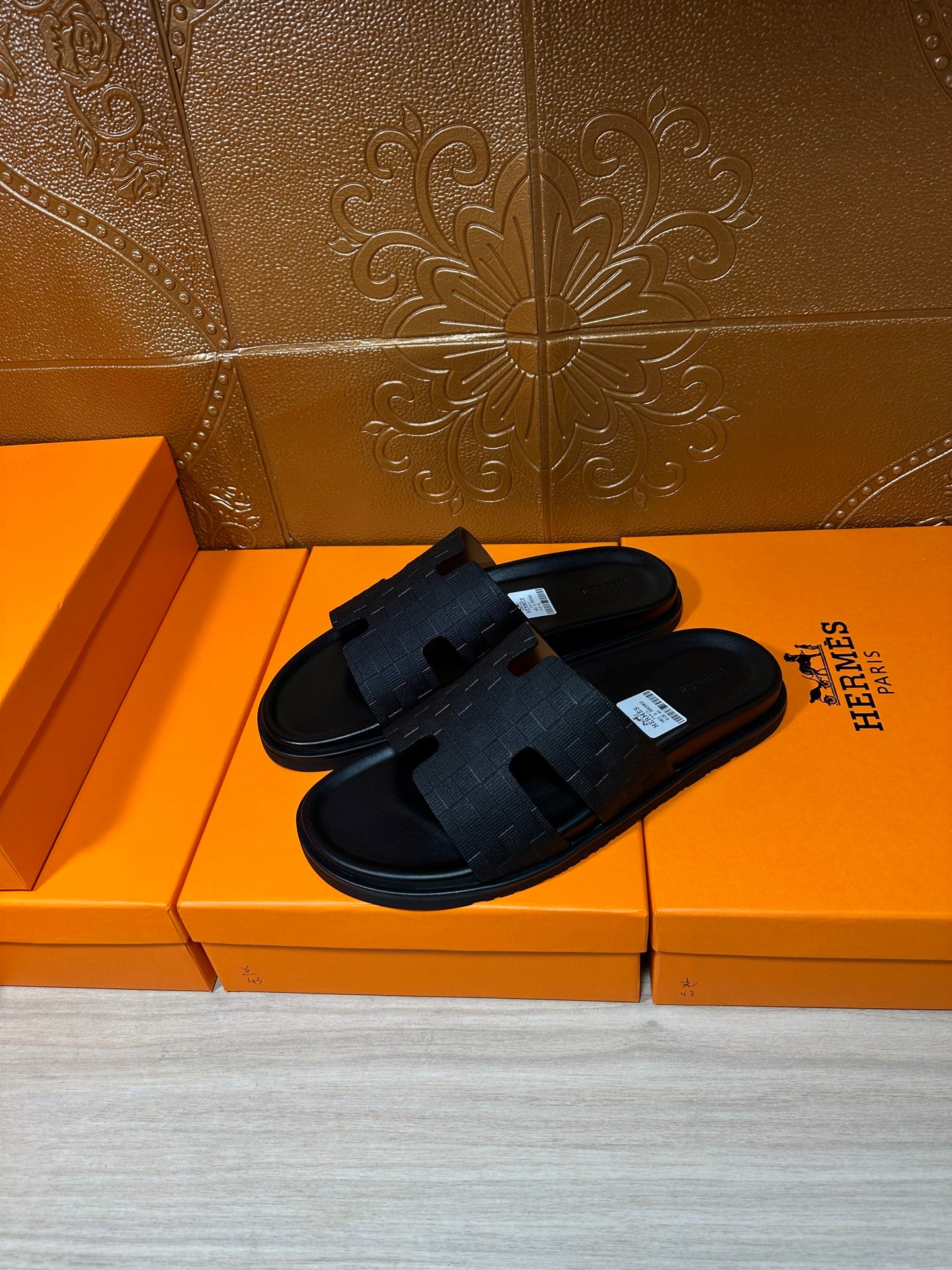 Black slide sandals with textured strap crossing and open-toe design, side view on box