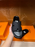 Black slide sandal held in hand, braided-pattern strap and contoured footbed