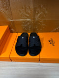 Black slide sandals with braided-pattern straps and open-toe design on orange box