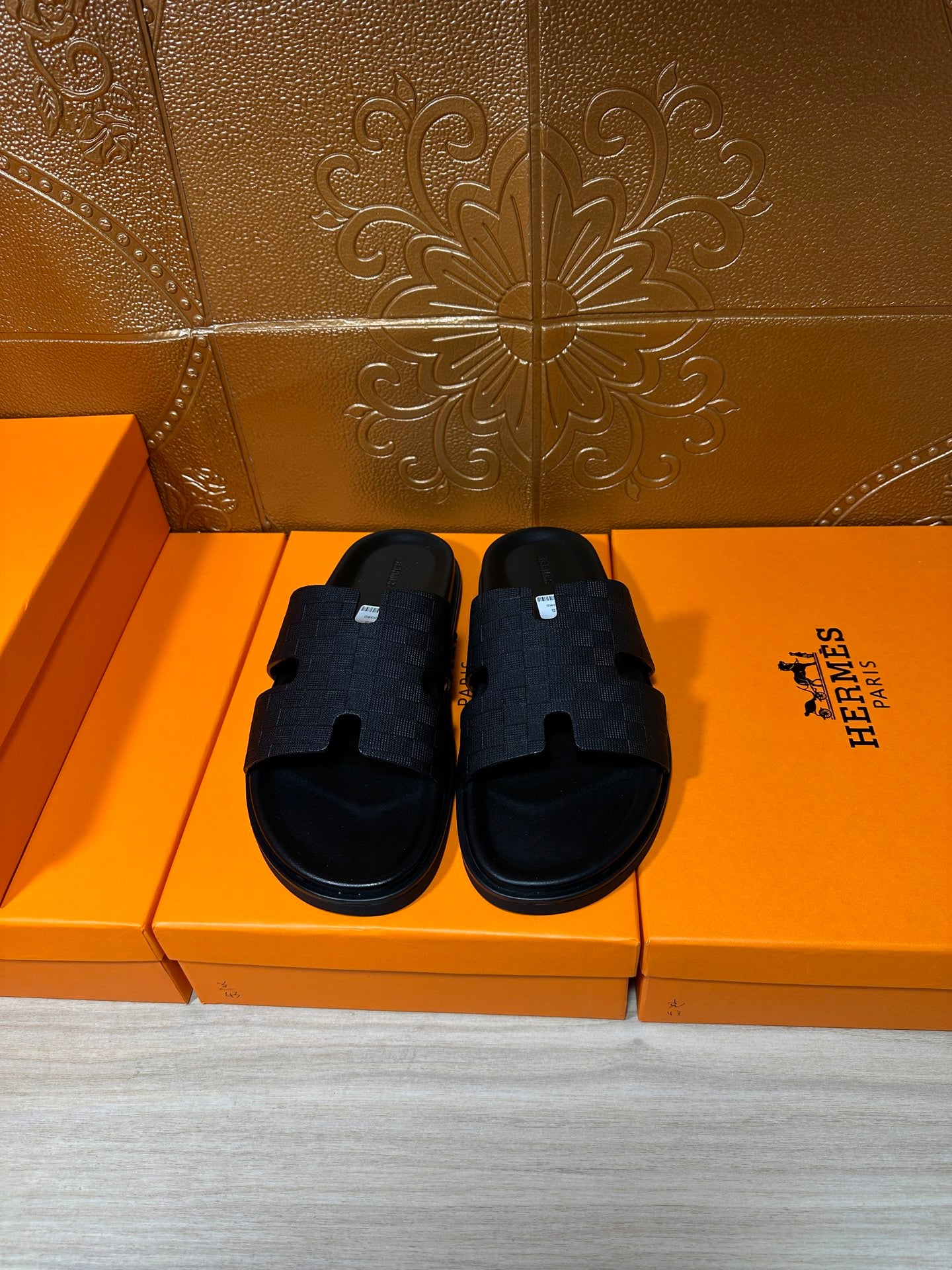 Black slide sandals with braided-pattern straps and open-toe design on orange box