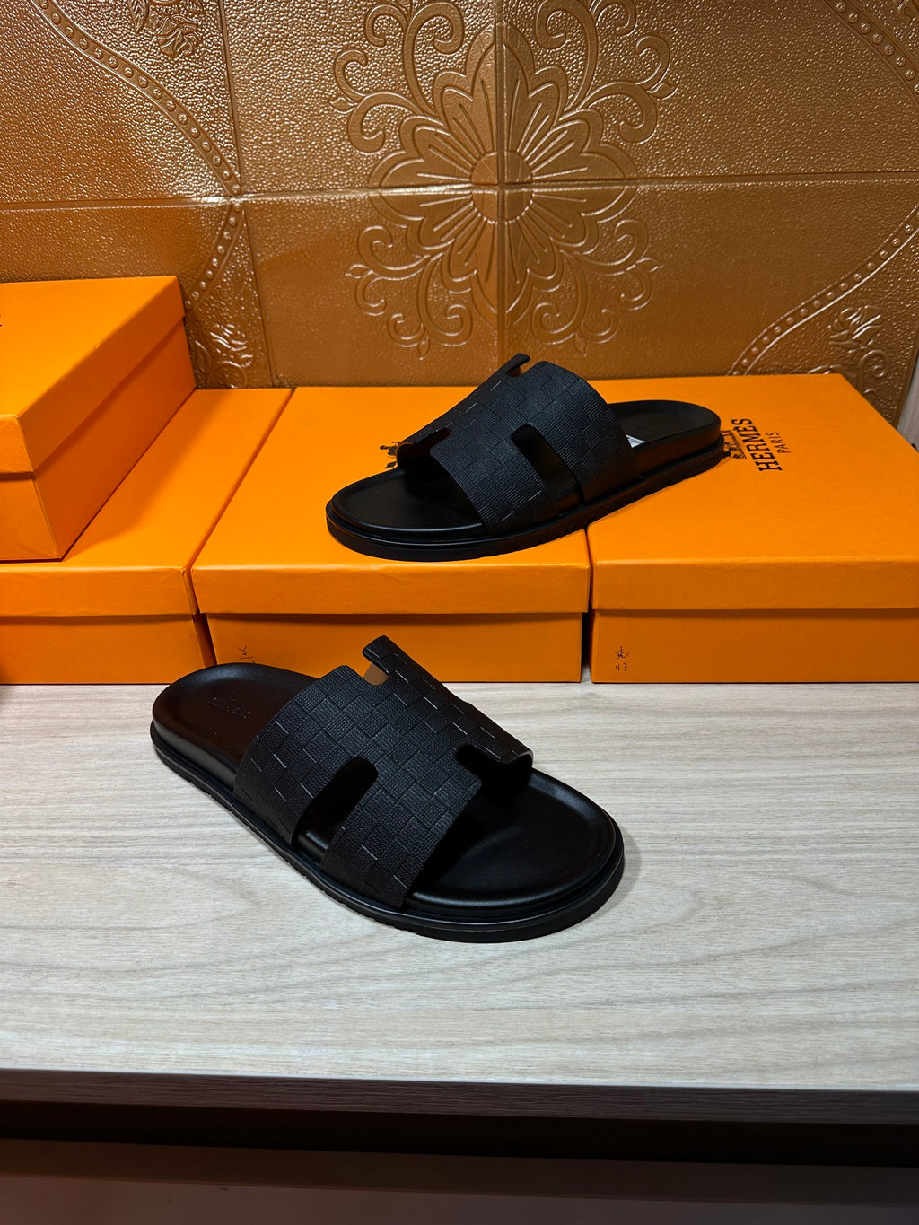 Black slide sandals pair on orange Hermes shoe boxes, open-toe slip-on style