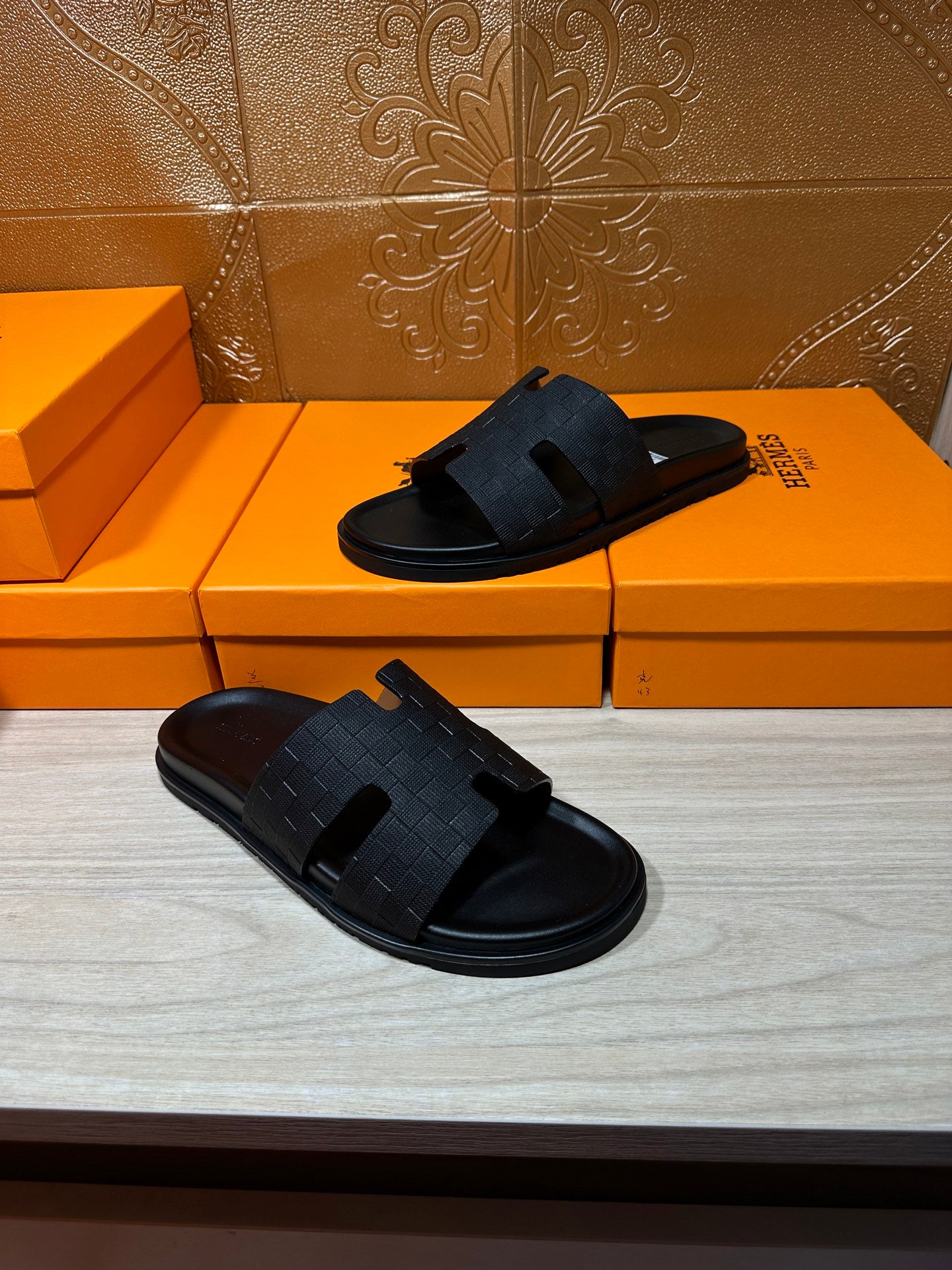 Black slide sandals pair on orange Hermes shoe boxes, open-toe slip-on style