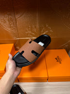 Hermes slide sandal close-up in hand, tan cross-strap on black sole