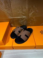 Hermes slide sandals showing tan cross-strap detail over black sole, angled view